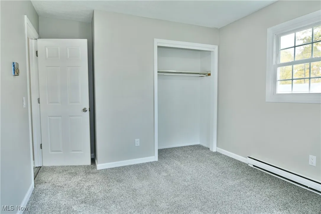 Unfurnished bedroom with light colored carpet, a baseboard heating unit, and a closet