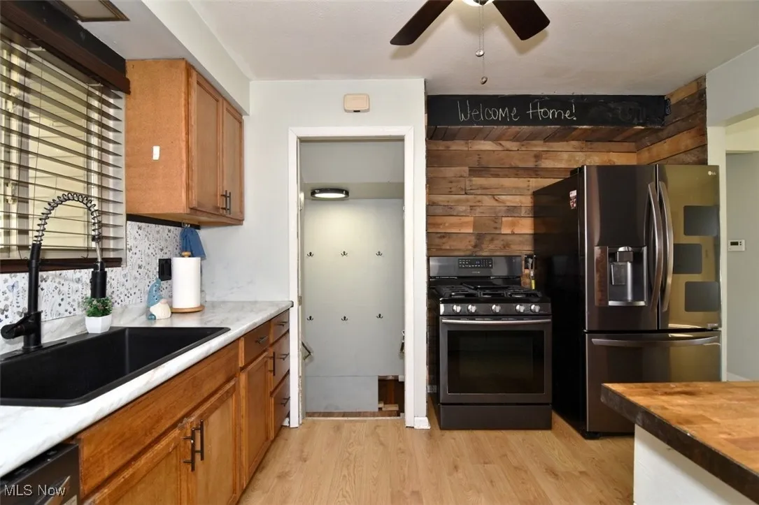 Kitchen featuring appliances with stainless steel finishes, light wood-type flooring, brown cabinetry, ceiling fan, and wood counters