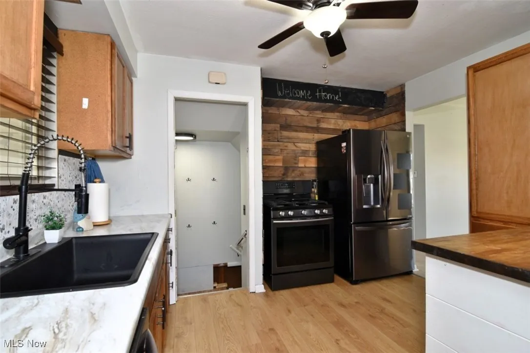 Kitchen with light wood-type flooring, stainless steel fridge, gas stove, backsplash, and ceiling fan
