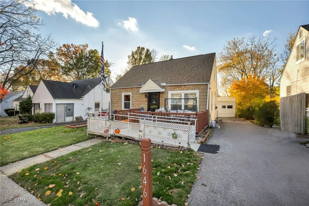 View of front of property featuring a front lawn, a deck, roof with shingles, stone siding, and garage