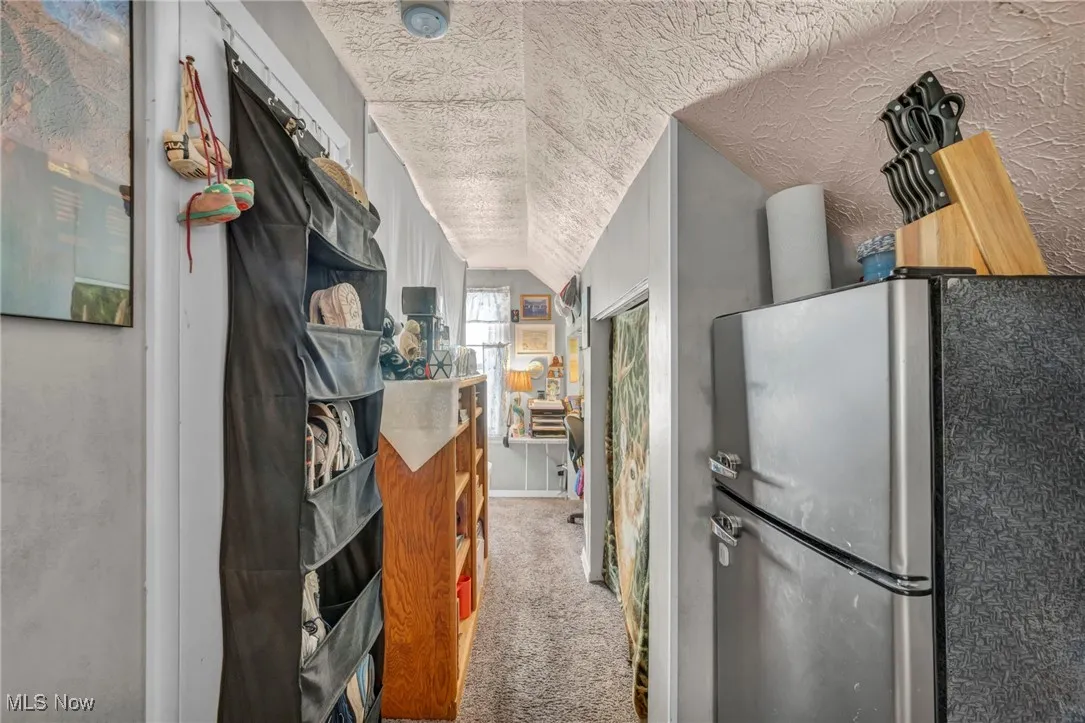 Hall with light carpet, a textured ceiling, and lofted ceiling