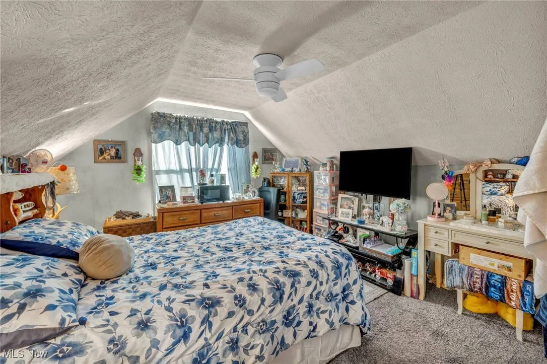 Carpeted bedroom with vaulted ceiling, ceiling fan, and a textured ceiling