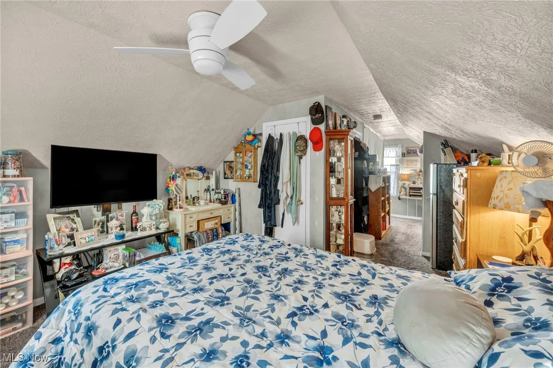 Carpeted bedroom with vaulted ceiling, a textured ceiling, and a ceiling fan