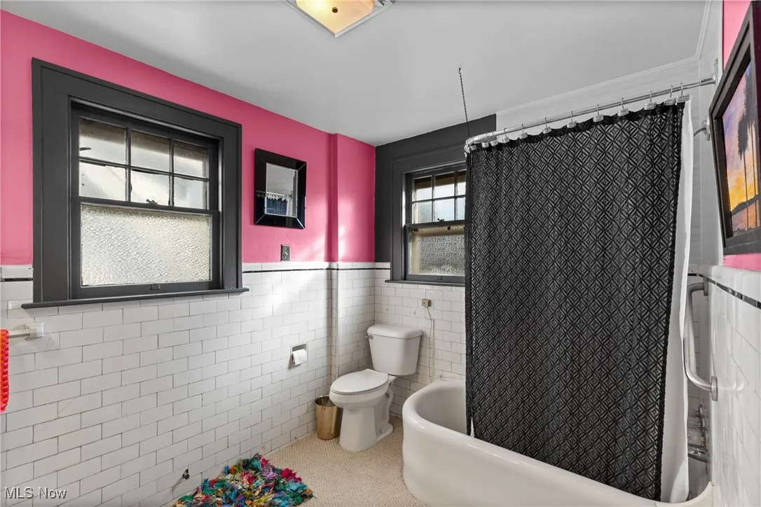 Bathroom featuring tile walls, wainscoting, and shower / bath combination with curtain
