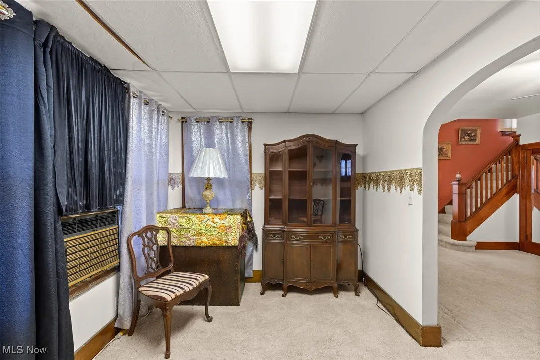 Living area featuring a paneled ceiling, arched walkways, light carpet, and stairway