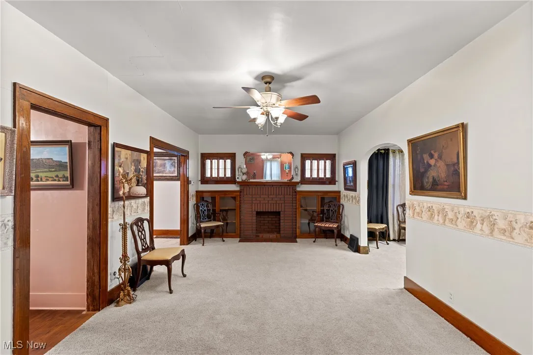 Living area featuring carpet floors, a fireplace, ceiling fan, and arched walkways