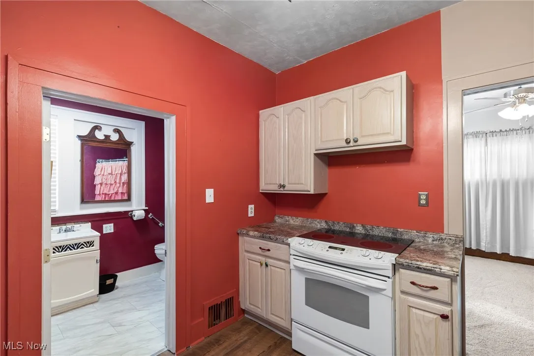 Kitchen featuring white electric range, a ceiling fan, dark wood-style floors, and dark stone counters