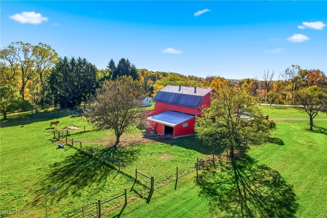 Aerial view of the scenic property showcasing the vibrant red barn, rolling green pastures, and mature trees. The expansive open space creates a serene country setting—perfect for equestrian activities, hobby farming, or simply enjoying peaceful rural living.