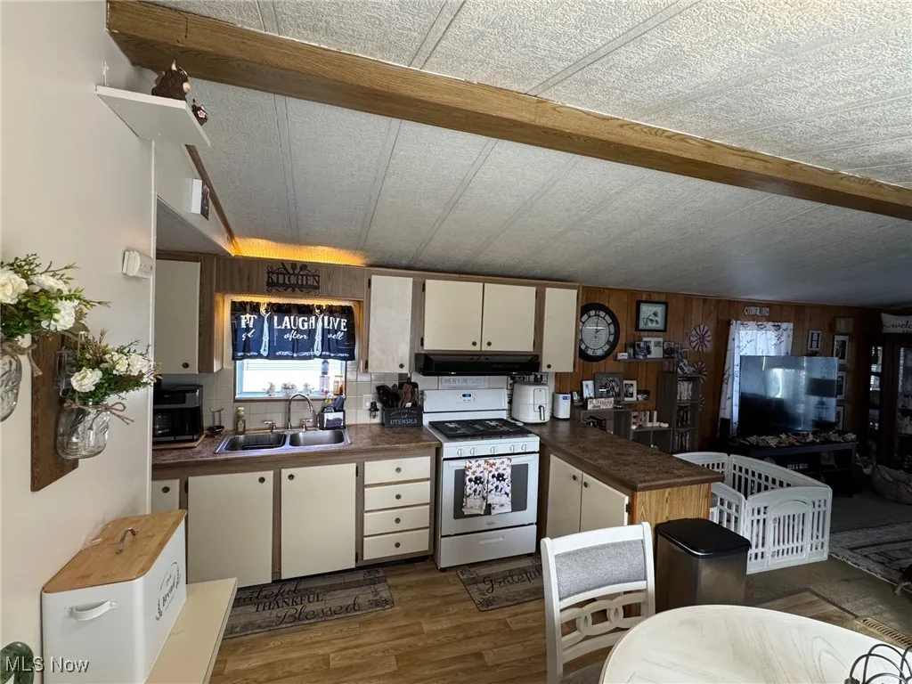 Kitchen featuring white gas range, dark wood-type flooring, white cabinets, a peninsula, and wooden walls
