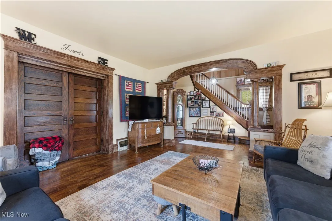 Living area with wood floors, decorative columns, stairs, and arched walkways