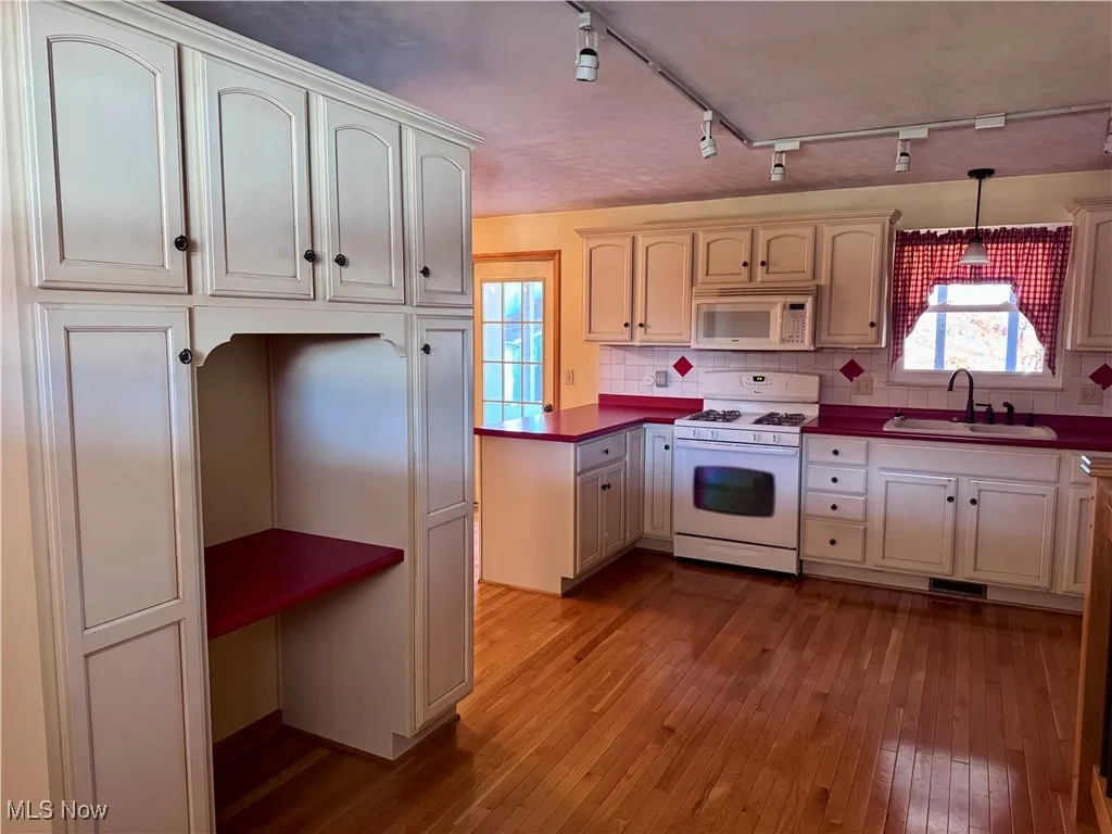 Kitchen with rail lighting, white appliances, tasteful backsplash, dark wood-style flooring, and dark countertops