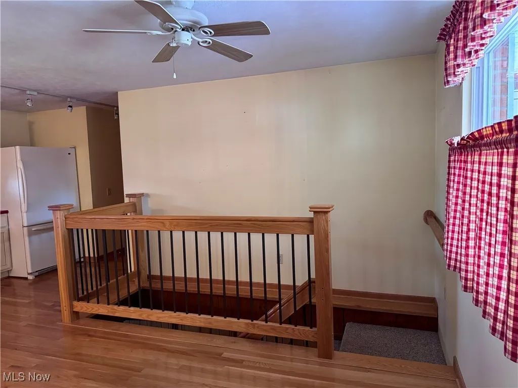 Stairway with wood finished floors, track lighting, and a ceiling fan
