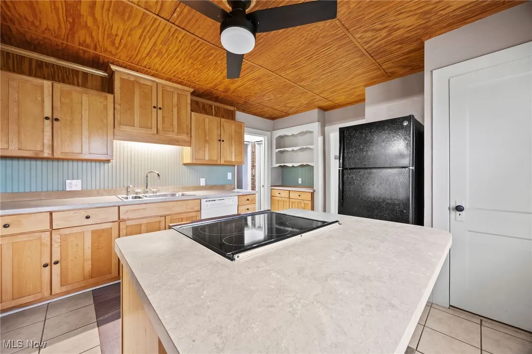 Kitchen with light countertops, light tile patterned flooring, black appliances, wooden ceiling, and a center island