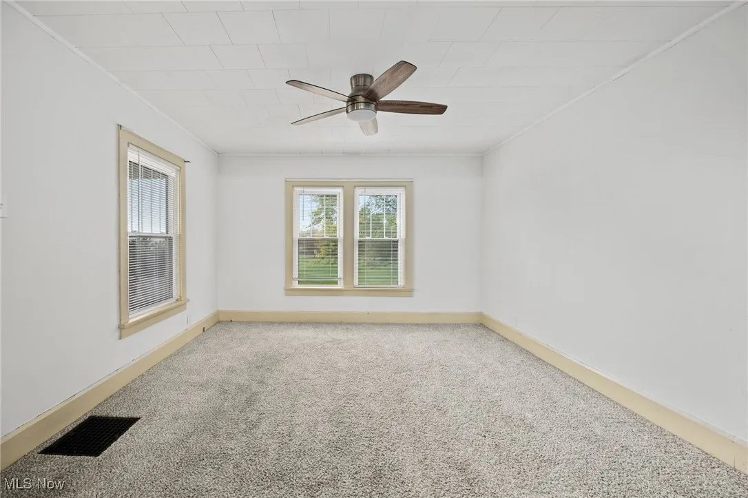 Carpeted empty room with ornamental molding and a ceiling fan