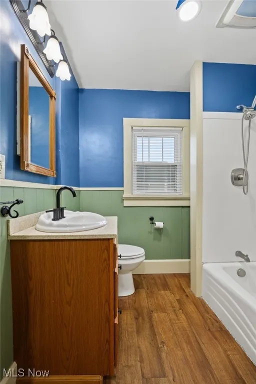 Bathroom with bathing tub / shower combination, vanity, dark wood-style floors, and wainscoting