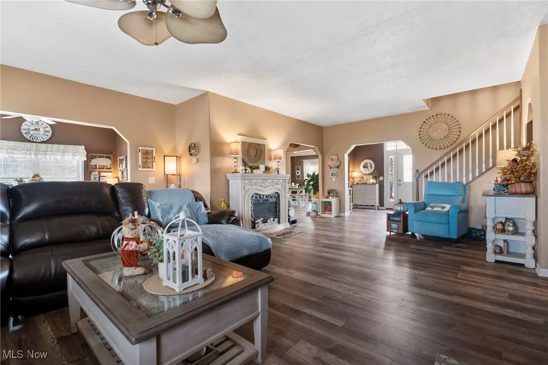 Living area featuring arched walkways, dark wood-style flooring, a fireplace, stairway, and a ceiling fan
