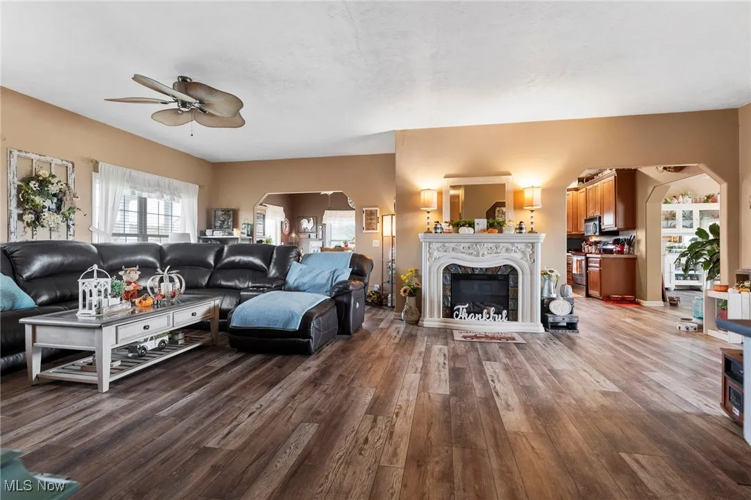 Living area with arched walkways, wood finished floors, a fireplace, and a ceiling fan