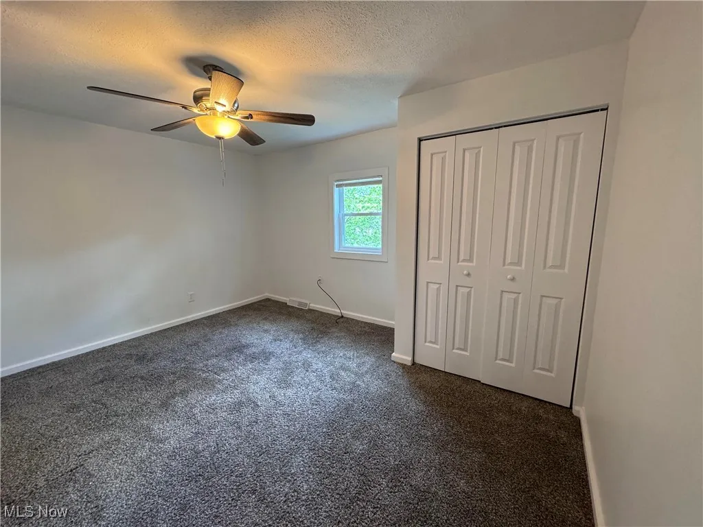 Unfurnished bedroom with dark carpet, a closet, ceiling fan, and a textured ceiling