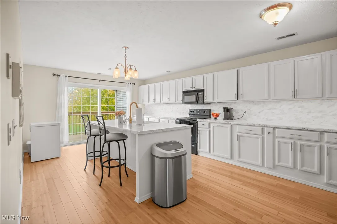 Kitchen with black appliances, pendant lighting, a kitchen breakfast bar, decorative backsplash, and white cabinetry