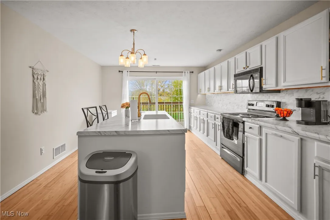 Kitchen with stainless steel electric stove, an island with sink, light wood-style flooring, tasteful backsplash, and decorative light fixtures