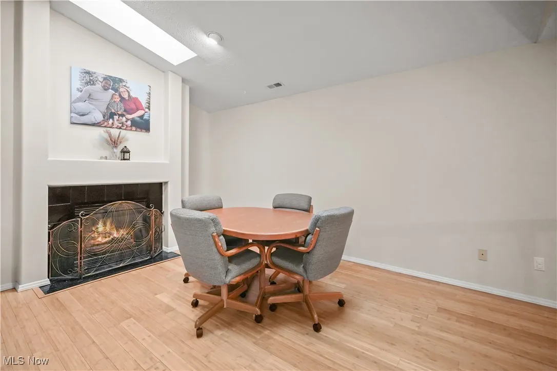 Dining area with a tiled fireplace, light wood finished floors, a skylight, and lofted ceiling