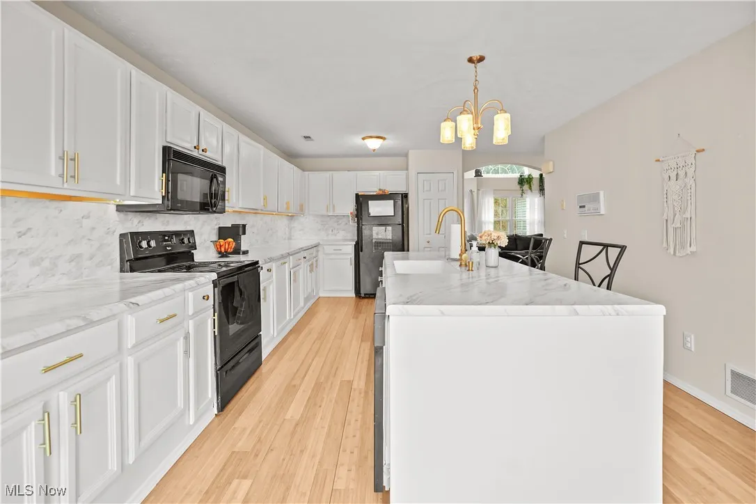 Kitchen featuring black appliances, white cabinetry, backsplash, decorative light fixtures, and light wood-type flooring