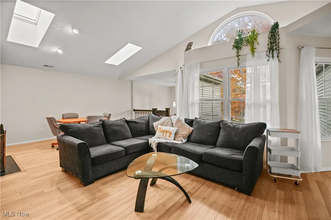 Living area with a skylight, high vaulted ceiling, and light wood finished floors