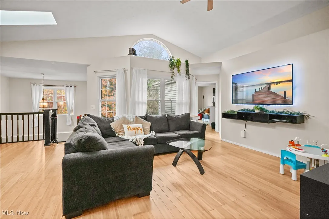 Living room with light wood finished floors, a skylight, ceiling fan, and high vaulted ceiling