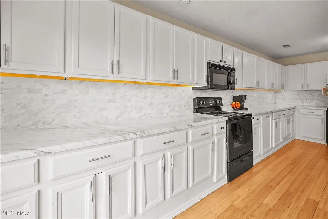 Kitchen with black appliances, white cabinetry, tasteful backsplash, light wood finished floors, and light stone counters
