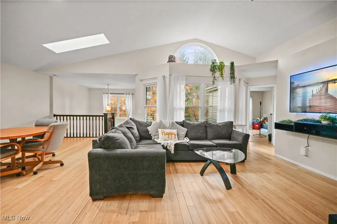 Living room with light wood-style flooring, a skylight, and high vaulted ceiling