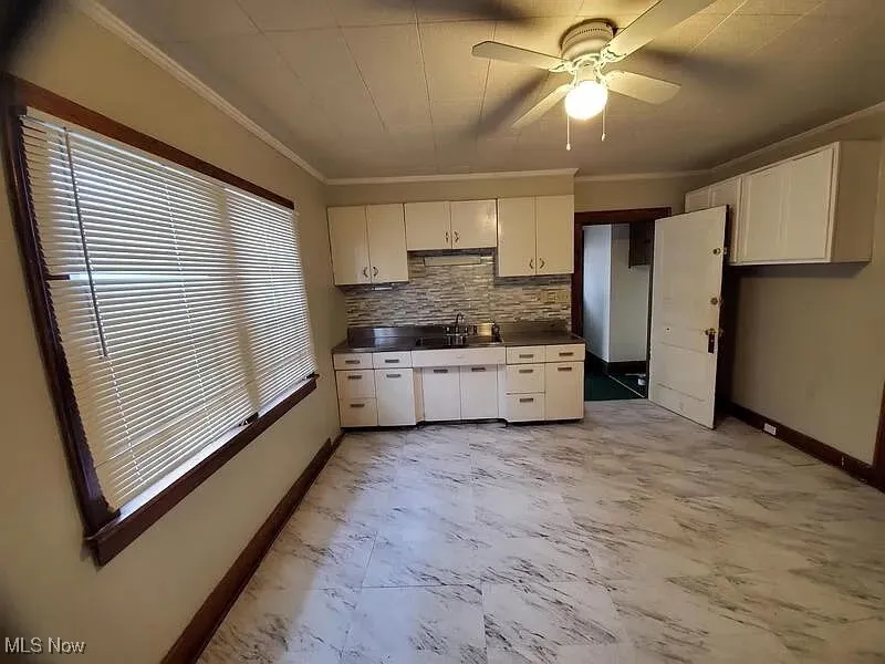 Kitchen featuring crown molding, dark countertops, decorative backsplash, white cabinets, and ceiling fan
