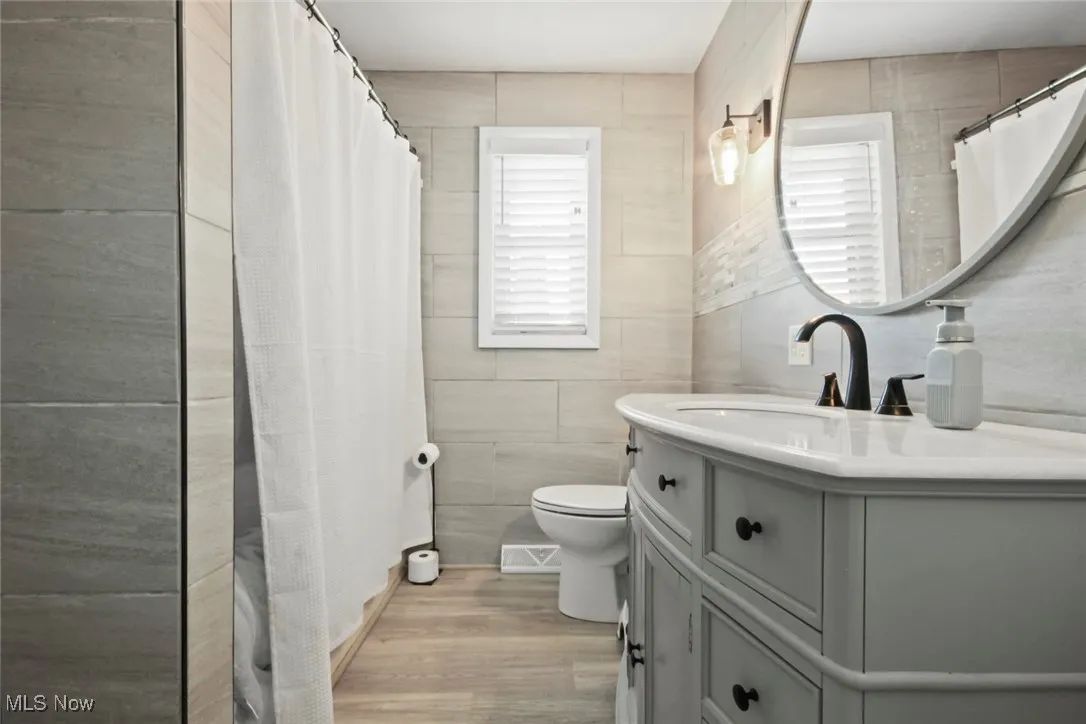 Full bath with tile walls, vanity, light wood-style flooring, and a shower with shower curtain