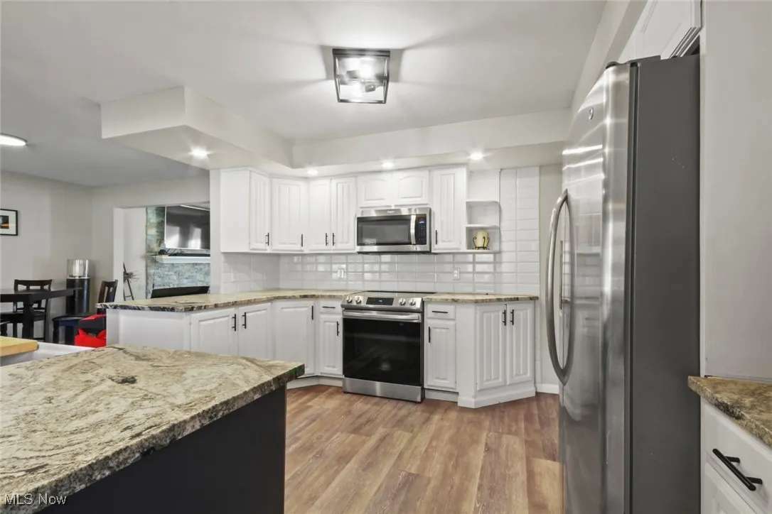 Kitchen with appliances with stainless steel finishes, white cabinets, decorative backsplash, light stone countertops, and light wood-type flooring