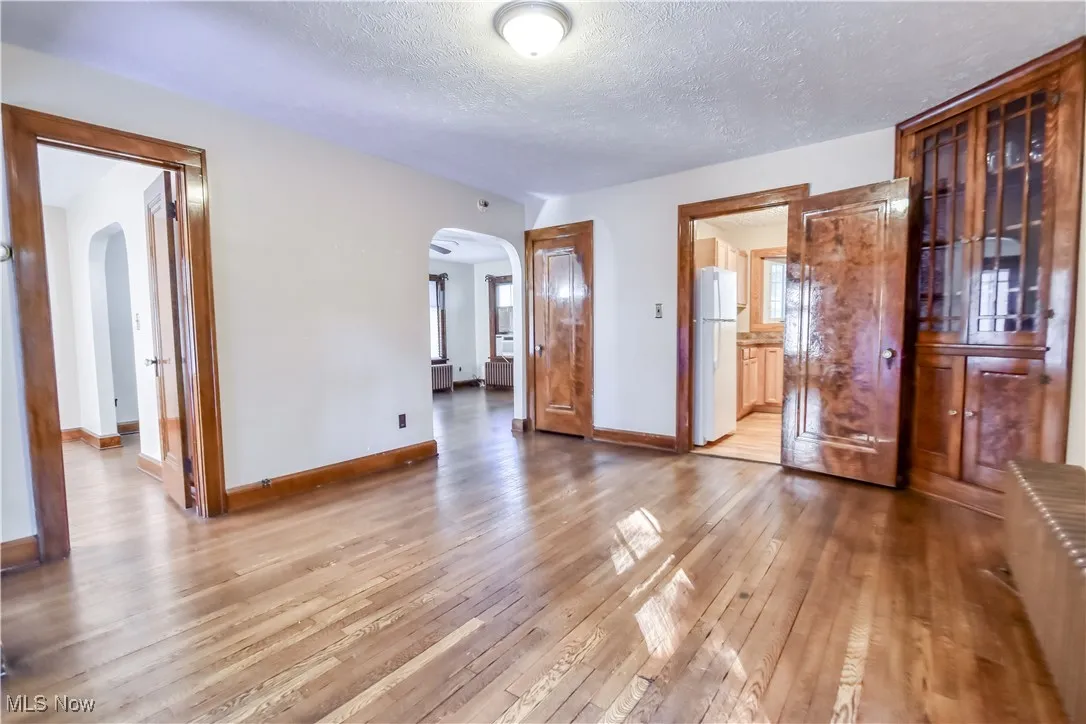Unfurnished bedroom featuring light wood-type flooring, freestanding refrigerator, a textured ceiling, and arched walkways