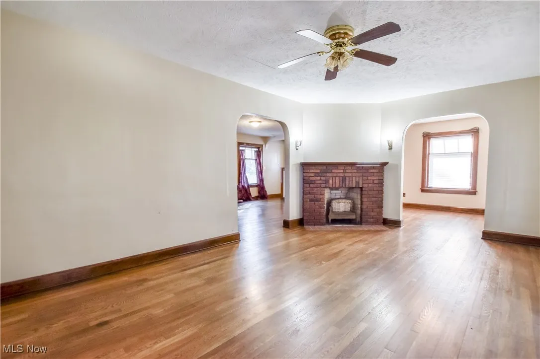 Unfurnished living room with ceiling fan, wood finished floors, a textured ceiling, healthy amount of natural light, and arched walkways