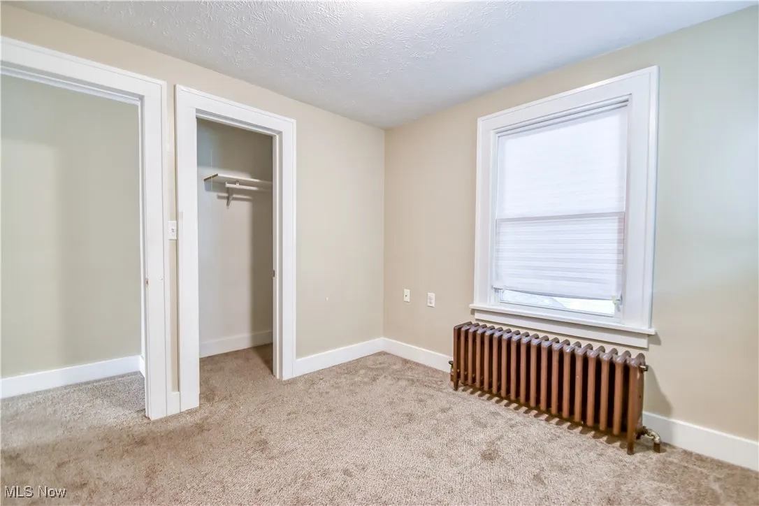 Unfurnished bedroom featuring radiator heating unit, light carpet, a textured ceiling, and a closet