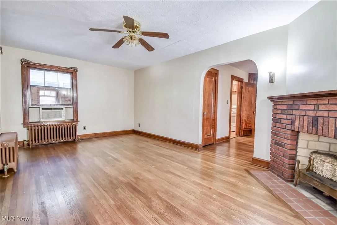 Unfurnished living room with wood finished floors, radiator, a textured ceiling, a fireplace, and a ceiling fan
