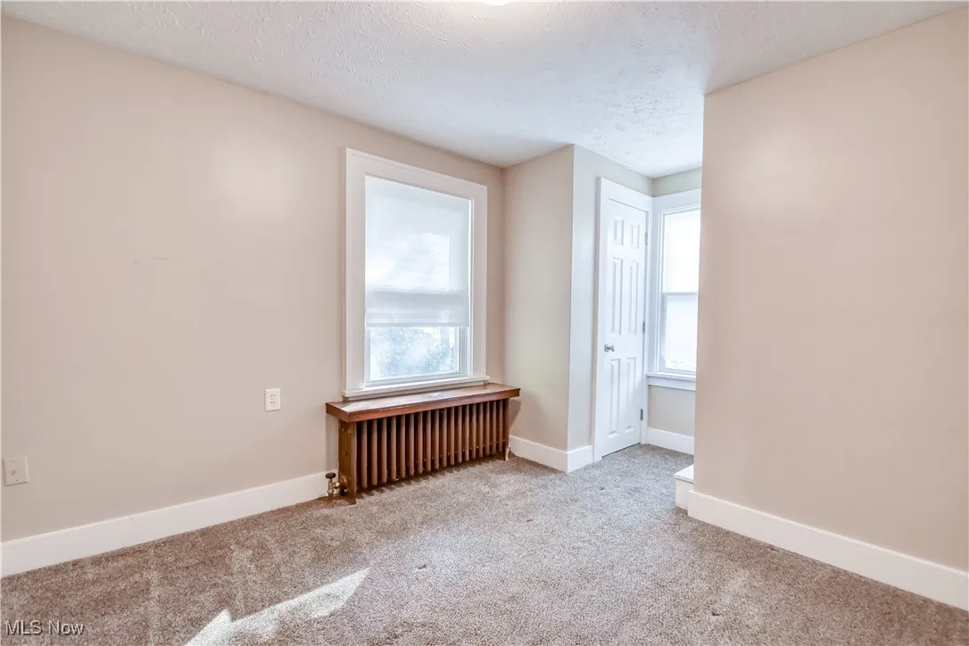 Carpeted spare room with radiator and a textured ceiling