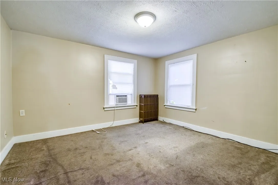 Carpeted empty room featuring radiator heating unit, a textured ceiling, and cooling unit