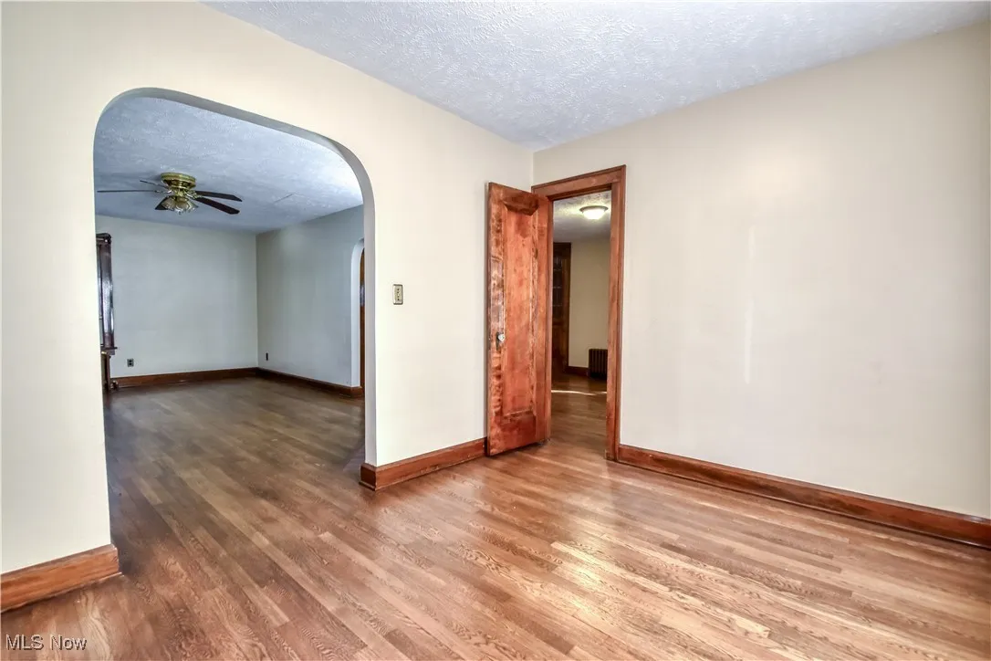 Unfurnished room with arched walkways, a textured ceiling, wood finished floors, and ceiling fan