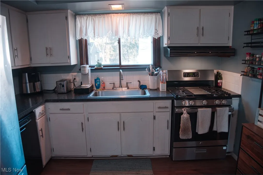 Kitchen with stainless steel gas stove, dark countertops, and white cabinetry