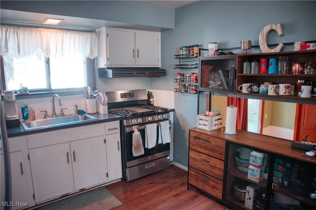 Kitchen with stainless steel range with gas cooktop, dark countertops, white cabinets, dark wood-type flooring, and ventilation hood