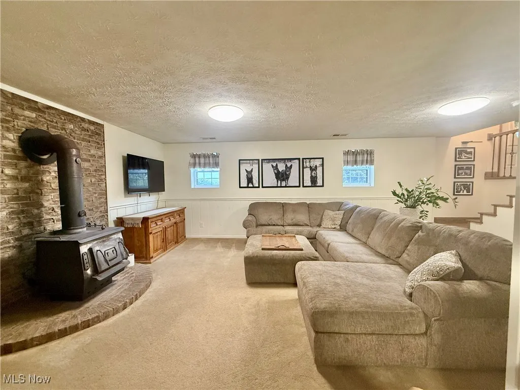 Living room with a wood stove, a textured ceiling, light carpet, wainscoting, and stairway