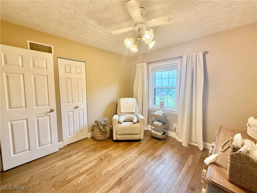 Living area with a textured ceiling, light wood-style flooring, and ceiling fan