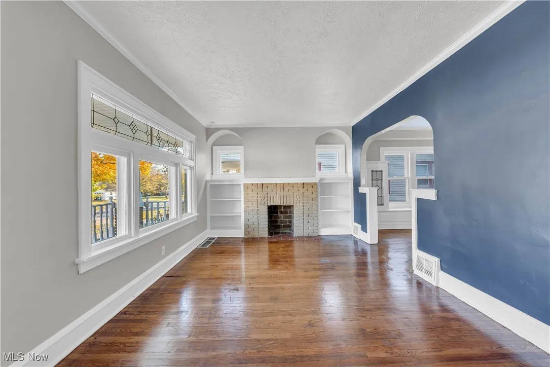 Unfurnished living room featuring a textured ceiling, dark wood-style floors, a fireplace with flush hearth, crown molding, and arched walkways