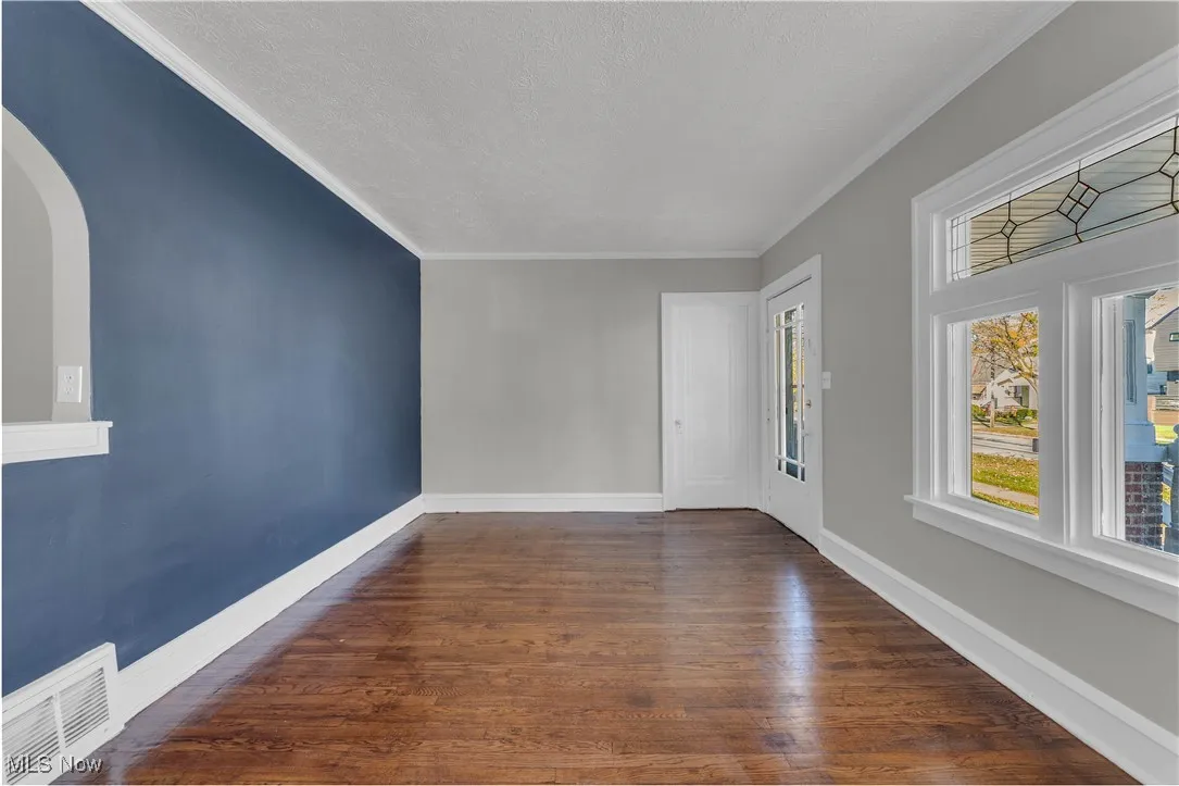 Spare room featuring crown molding, dark wood-style flooring, a textured ceiling, and arched walkways