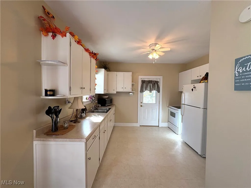 Kitchen featuring appliances, light countertops, white cabinetry, and a ceiling fan