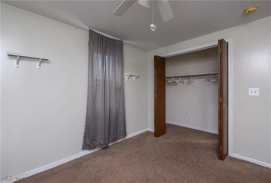 Unfurnished bedroom with carpet floors, a textured ceiling, a closet, and ceiling fan