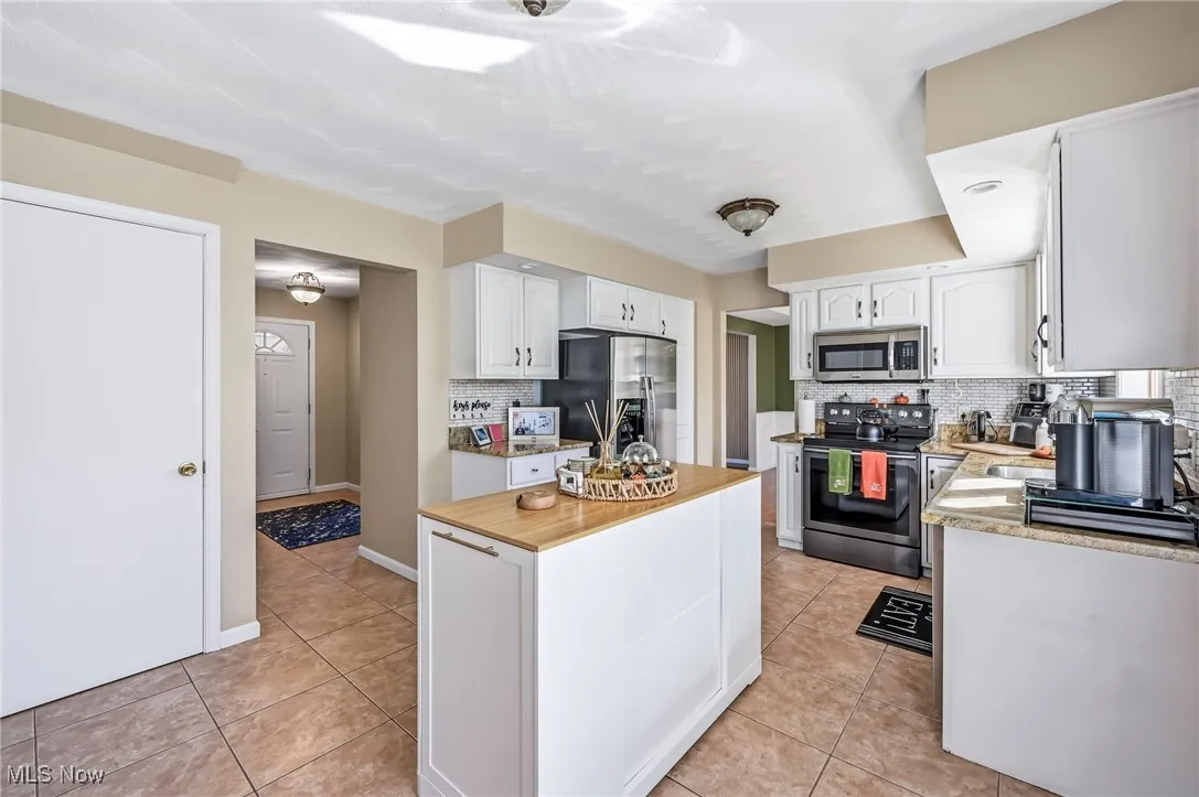 Kitchen with butcher block counters, stainless steel appliances, light tile patterned flooring, and white cabinets