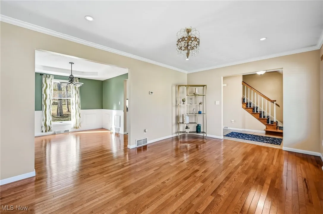 Unfurnished living room with a chandelier, light wood-type flooring, crown molding, stairs, and recessed lighting